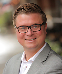 blonde man in suit, smiling with glasses